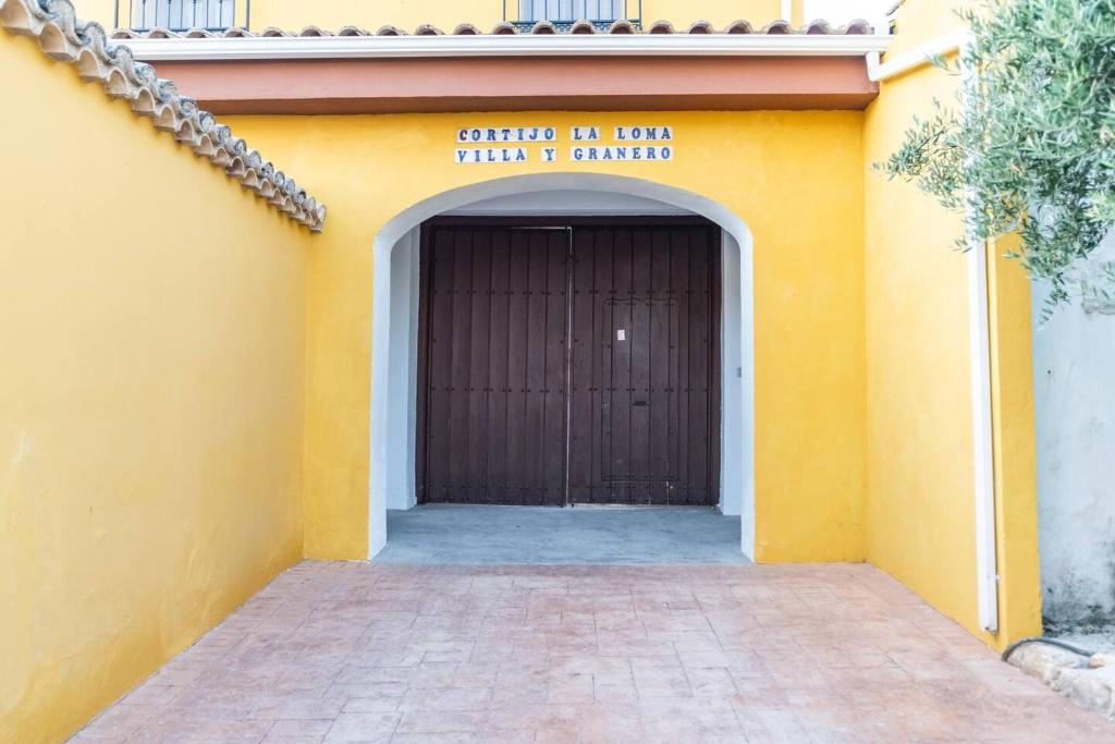 un edificio amarillo con garaje con puerta marrón en Casa Rural "compartida" La Loma Granero, en Granada