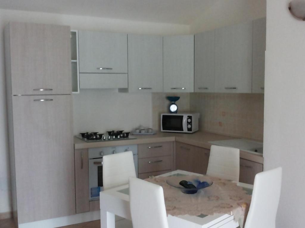 uma cozinha com armários brancos e uma mesa e cadeiras em Appartamenti Isola Rossa em Valledoria
