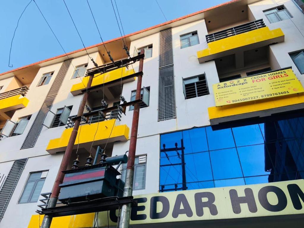 a building with yellow windows and a sign on it at Abuzz Oxfordcaps Cedar Homes in Jhājra