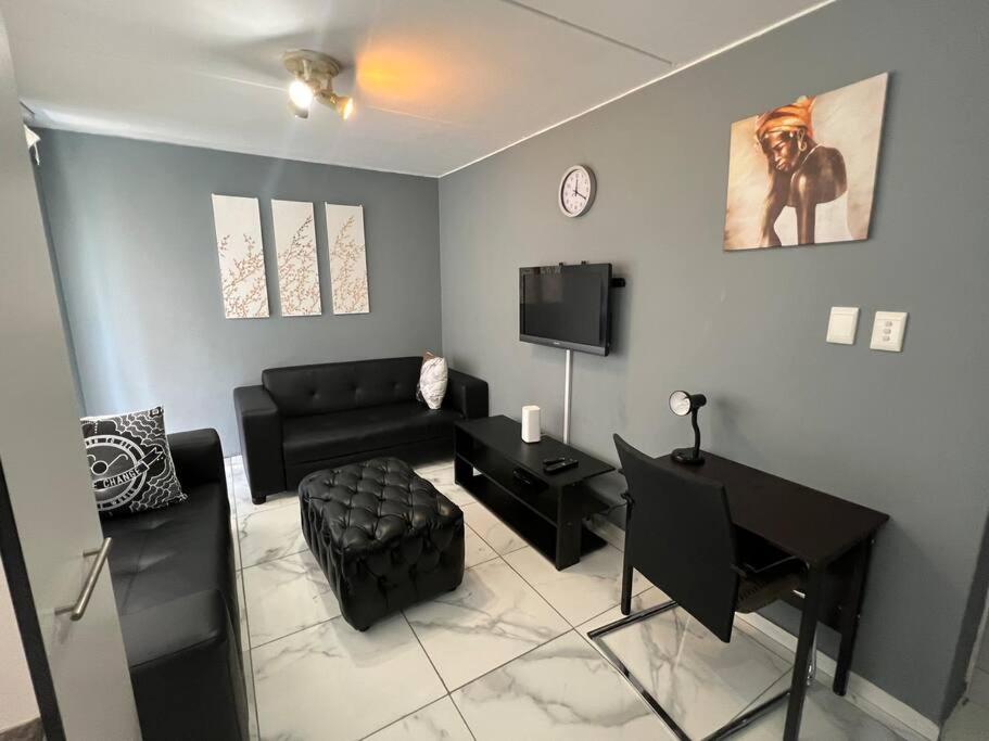 a living room with a black couch and a television at Beyond Comfort Apartment in Pretoria