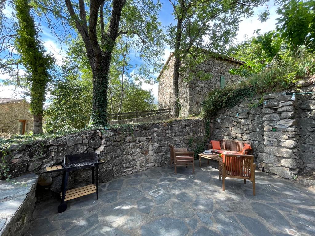 uma parede de pedra com cadeiras, uma mesa e um grelhador em L'Oustal de la Calade em Valleraugue