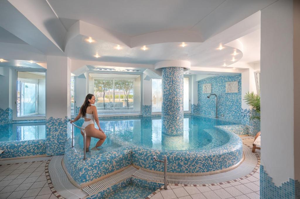 una donna in costume da bagno in piedi sul bordo di una piscina di Hotel Baia Imperiale a Rimini