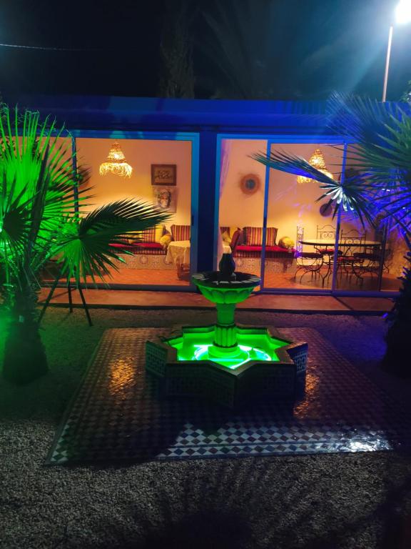Petit paradis في Sidi Bibi: وجود نافورة خضراء أمام المنزل ليلاً