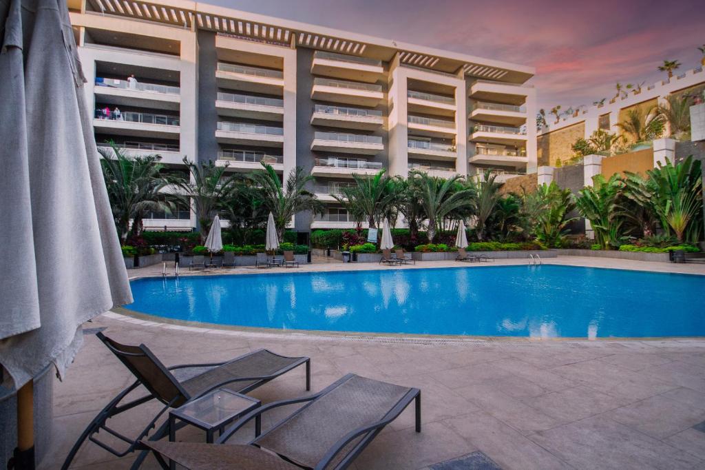 una piscina con 2 sillas y un edificio en Hotel exceptional luxury apartments next to Cairo airport at ocean blue compound Heliopolis en El Cairo