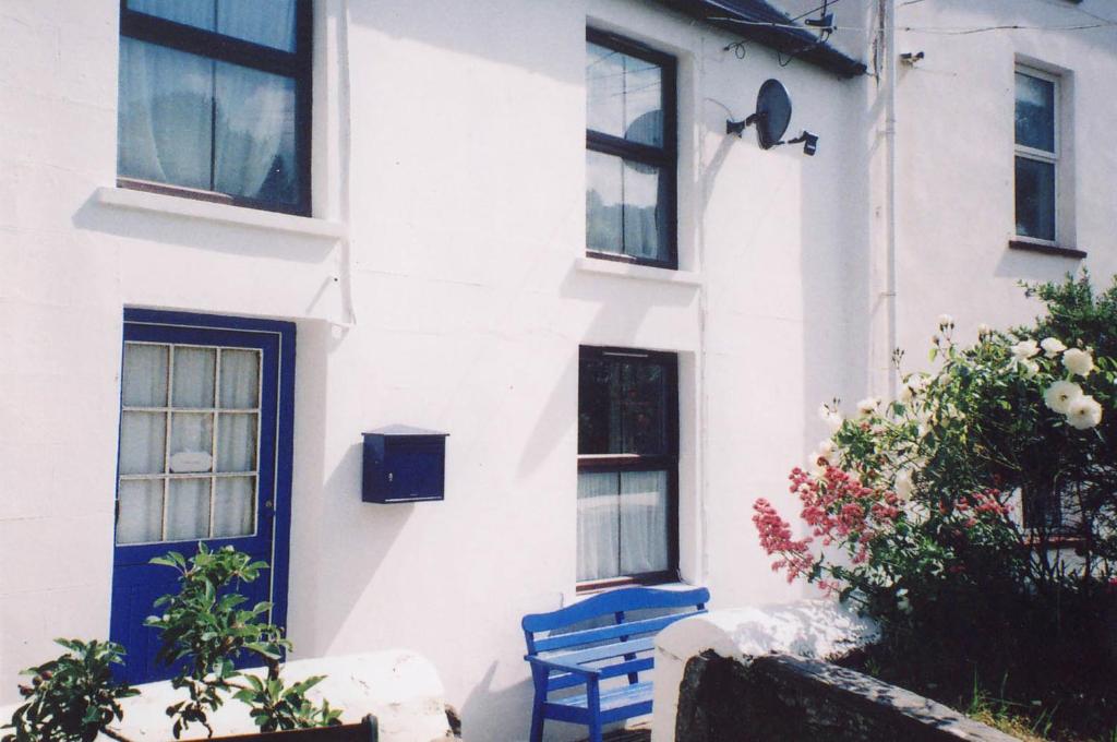 Uma casa branca com um banco azul à frente. em 2 Castle Hall Llangrannog em Llangranog