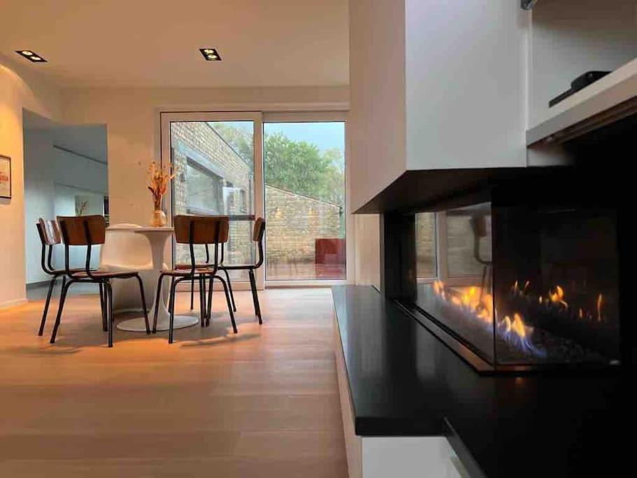 a living room with a fireplace and a table and chairs at Gezellig huis met open haard en fenomenale tuin in Koksijde
