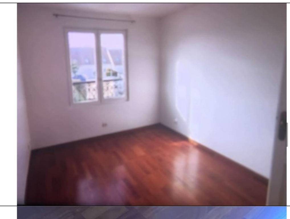 uma sala de estar vazia com uma janela e pisos em madeira em Le Rosiers em Poissy