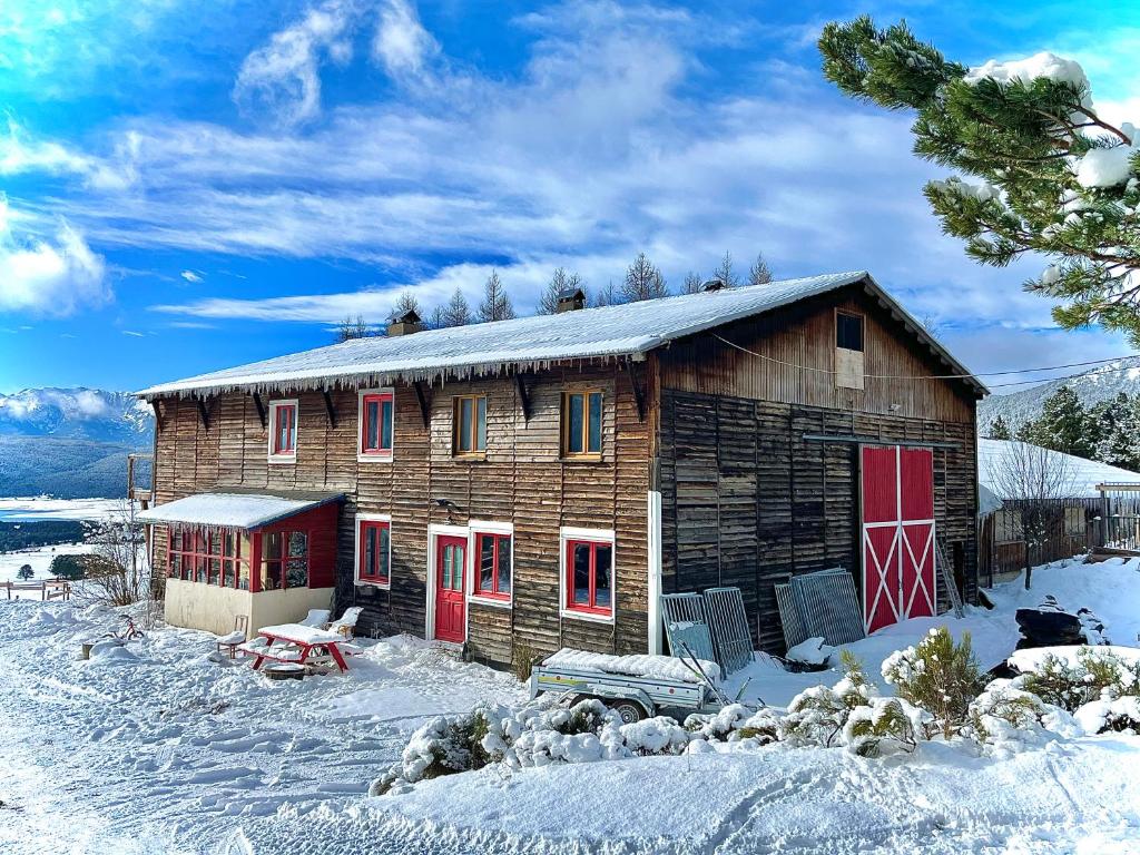 a wooden cabin with red doors in the snow at Gîte Ranch Le Serpolet in Les Angles
