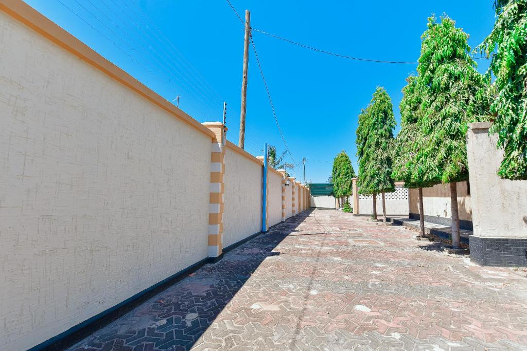 un long trottoir à côté d'un mur blanc avec des arbres dans l'établissement GOWON BnB, à Bunju