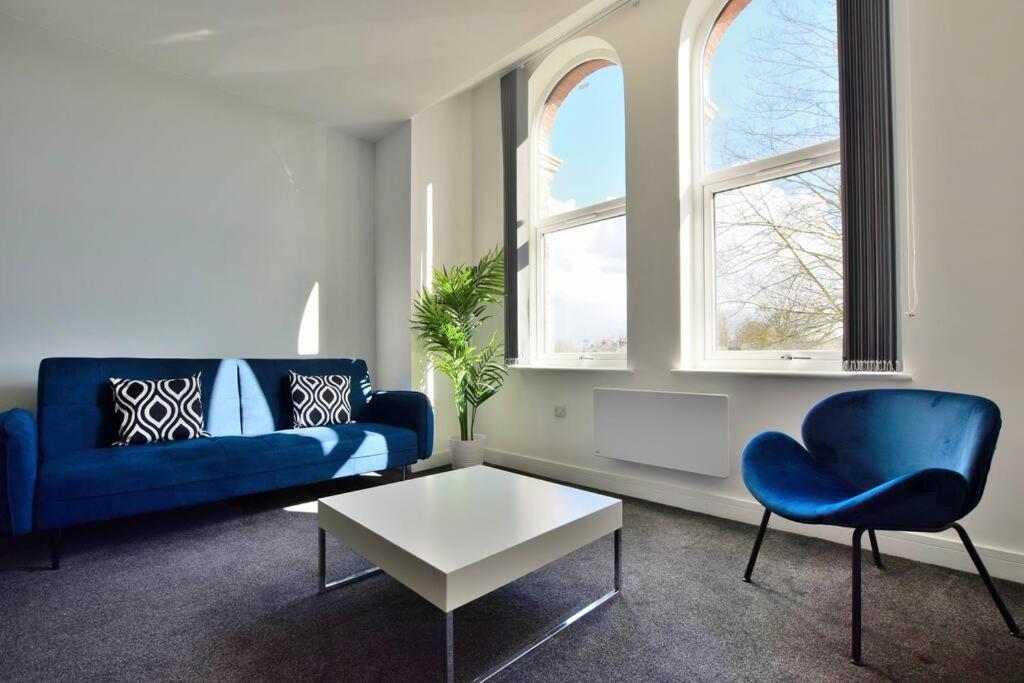 ein Wohnzimmer mit einem blauen Sofa, einem Tisch und 2 Fenstern in der Unterkunft FREE PARKING - Beautiful 2-BR Flat in Manchester in Manchester