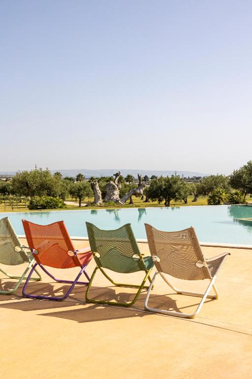 trzy krzesła ogrodowe siedzące przed basenem w obiekcie Agua Green Resort w mieście Reitani