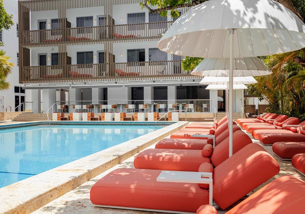 a row of lounge chairs with an umbrella next to a swimming pool at Axel Beach Miami-South Beach - Adults Only in Miami Beach