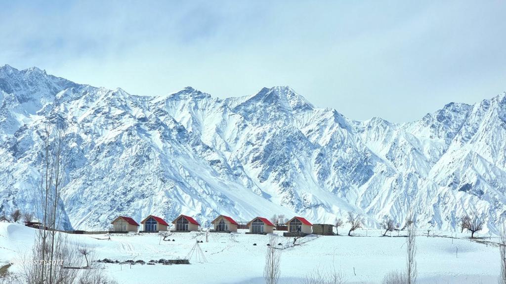 a snow covered mountain with a group of red buildings at Oasis Resort in Skardu