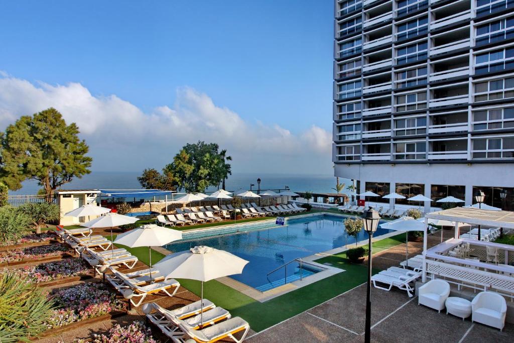 una piscina con sillas y sombrillas junto a un edificio en The Seasons Hotel -Studio & Suite, en Netanya