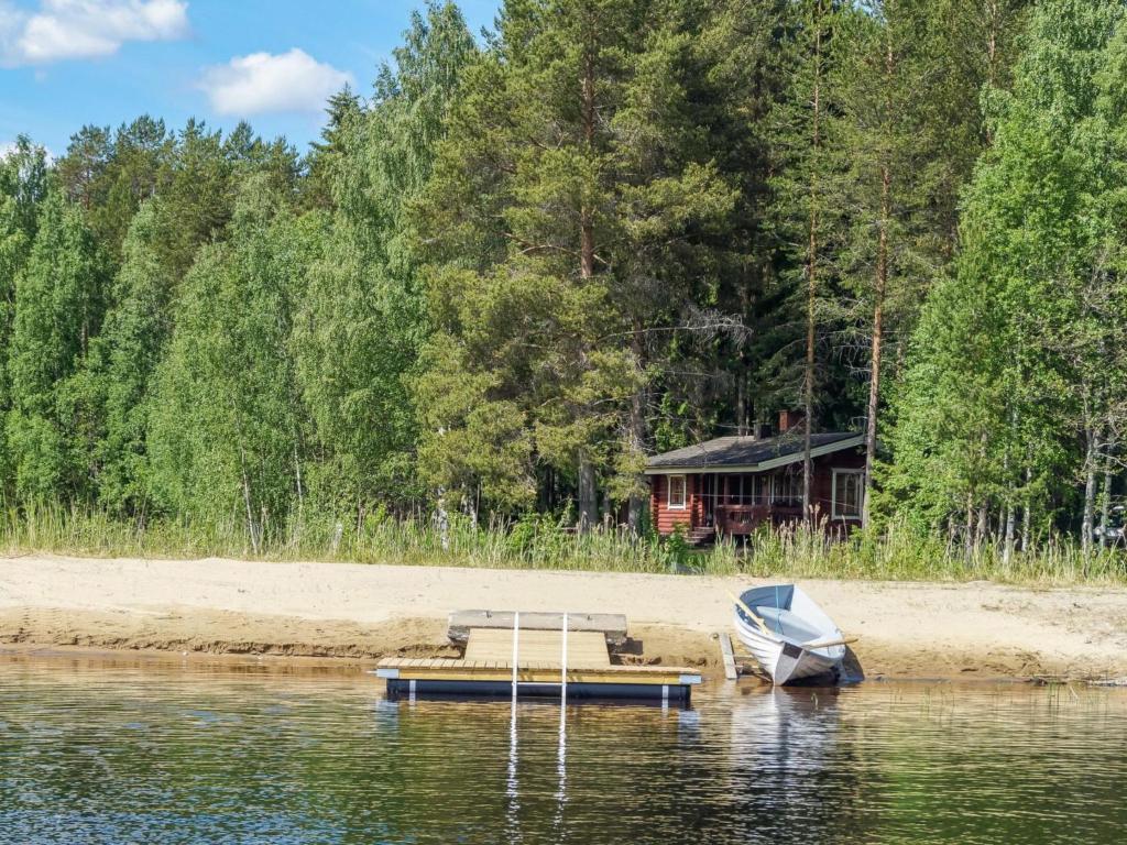 a boat and a house on the shore of a lake at Holiday Home Huvilakoti 2 by Interhome in Puromäki