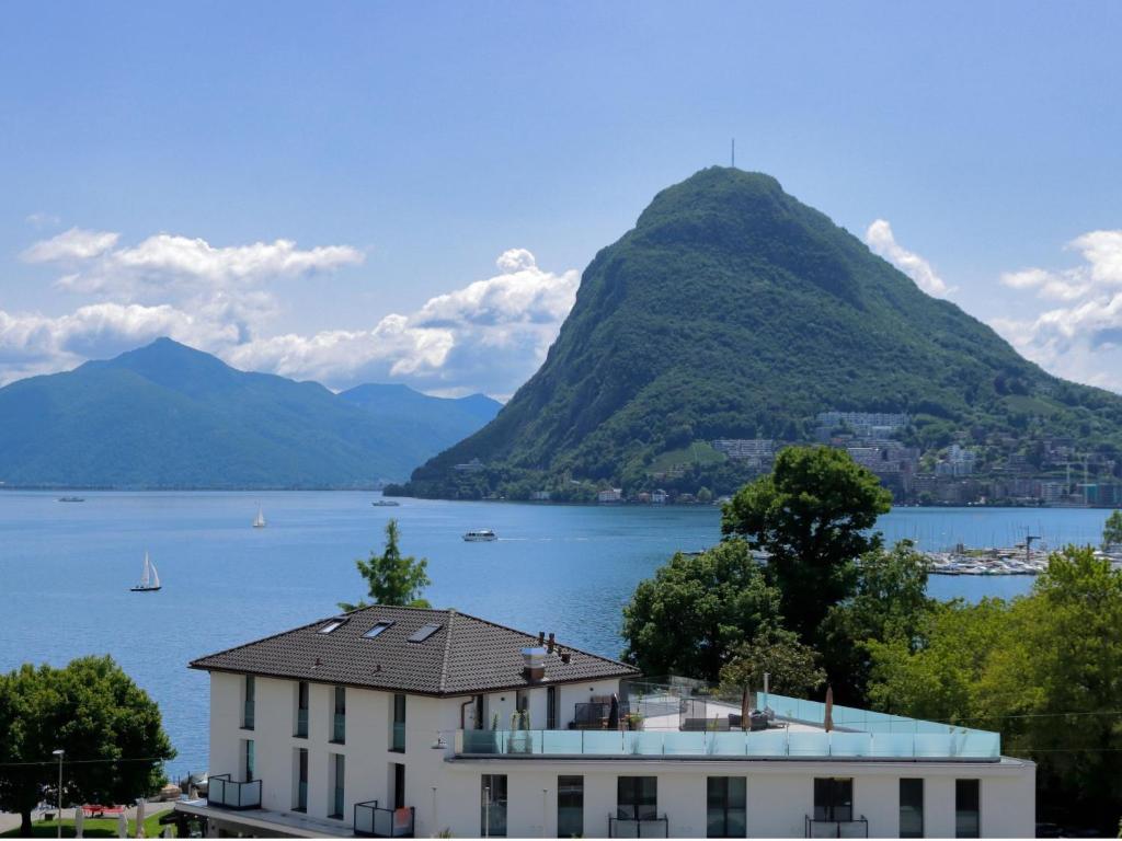 a house in front of a mountain with a body of water at Apartment Residenza Cassarate Lago-1 in Lugano