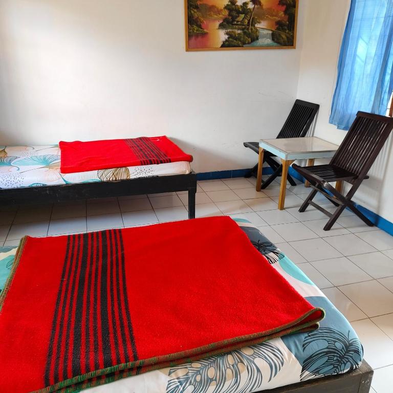 a room with two beds and a table and a red rug at Volcano Bali House in Kubupenlokan