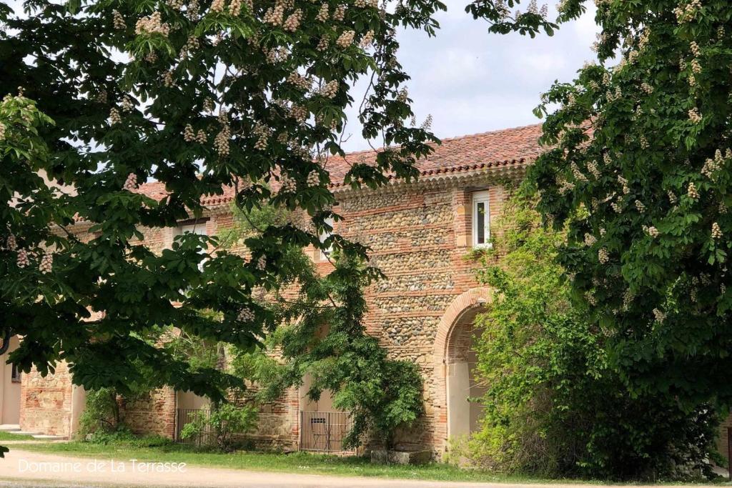 un bâtiment en briques avec une grande porte et des arbres dans l'établissement Domaine de la Terrasse, à Carbonne