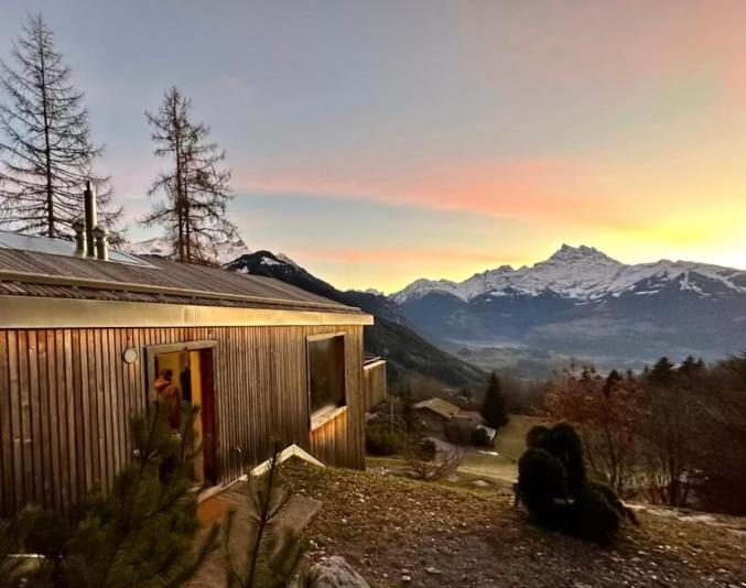 a person sitting outside of a house with mountains in the background at Chalet contemporain in Gryon