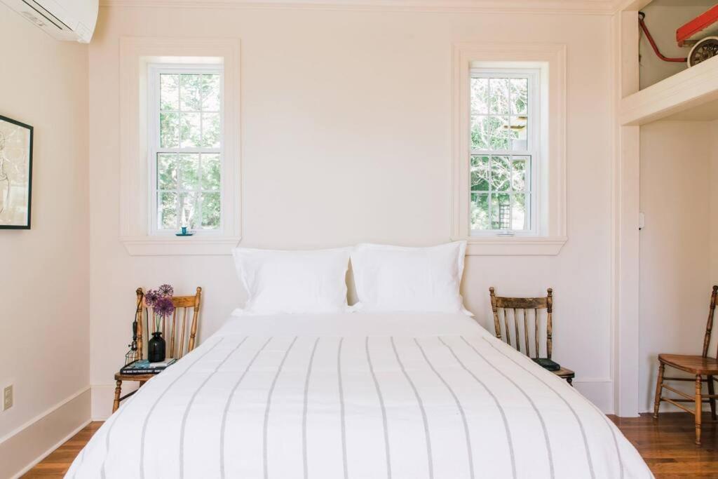 uma cama branca num quarto com duas janelas em The Schoolhouse PEC + Sandbanks Parking Pass em Demorestville