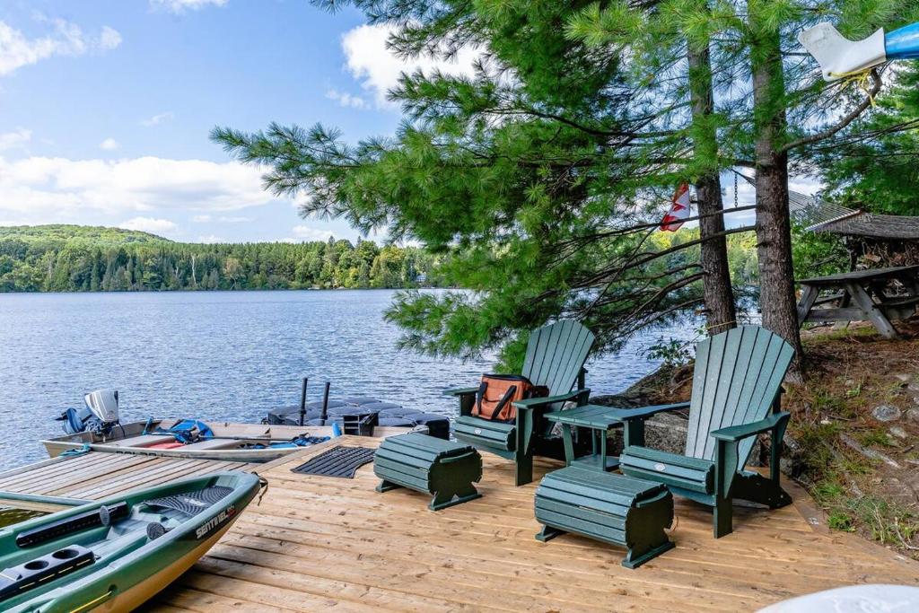 a dock with chairs and a boat on a lake at Entire cottage in Algonquin Highlands Canada in Algonquin Highlands