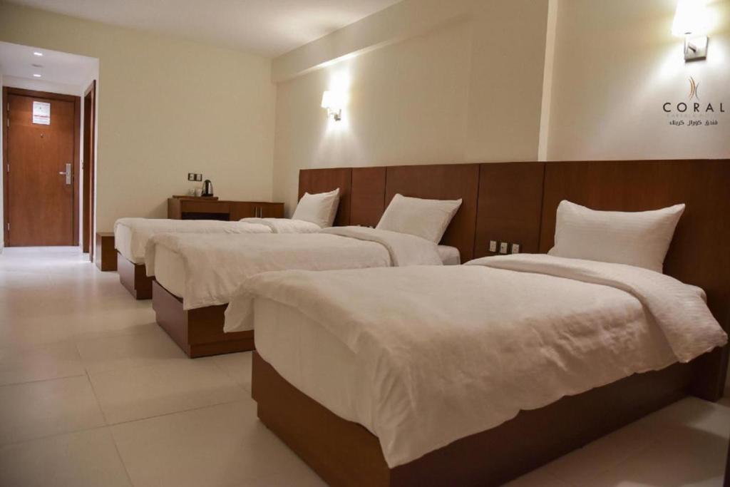 a hotel room with three beds with white sheets at Coral Hotel Karbala in Karbalāʼ