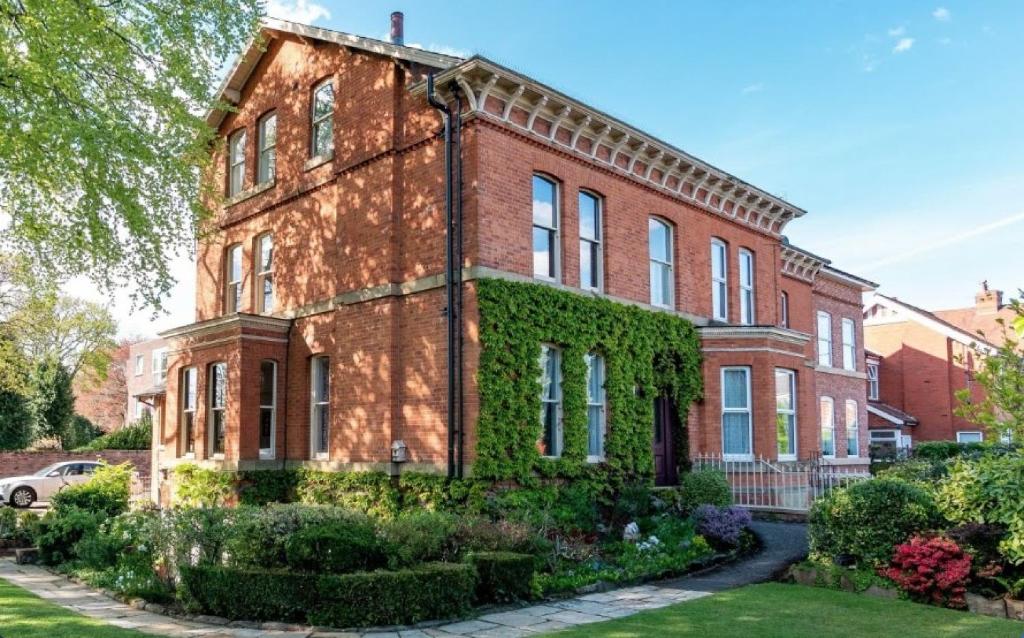 an old brick building with ivy on it at Cornerstones Guest House in Sale