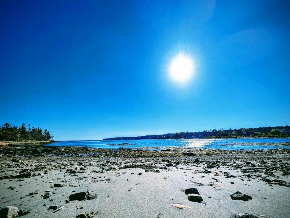 a beach with rocks and the sun in the sky at Beachy Watering Cove Cottage NEW in Prospect Harbor