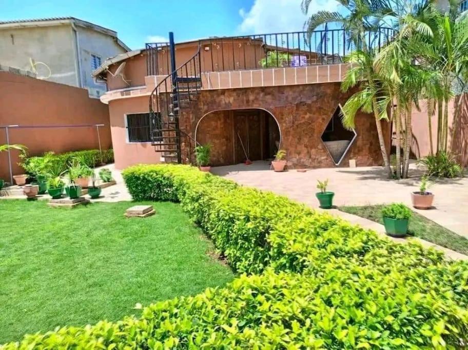 une arrière-cour avec une maison avec une pelouse et des arbres dans l'établissement Élégante villa avec jardin+bar, à Lomé