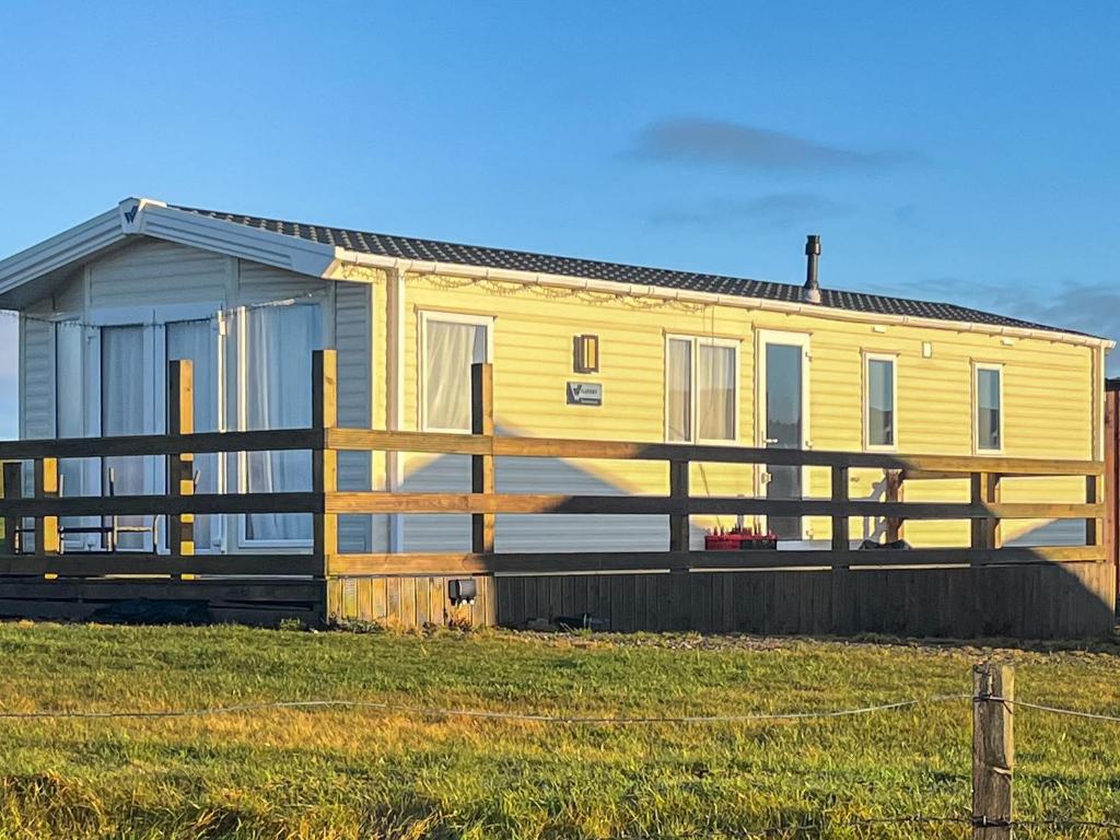 a yellow house with a fence in a field at Woodend Caravan in Lairg