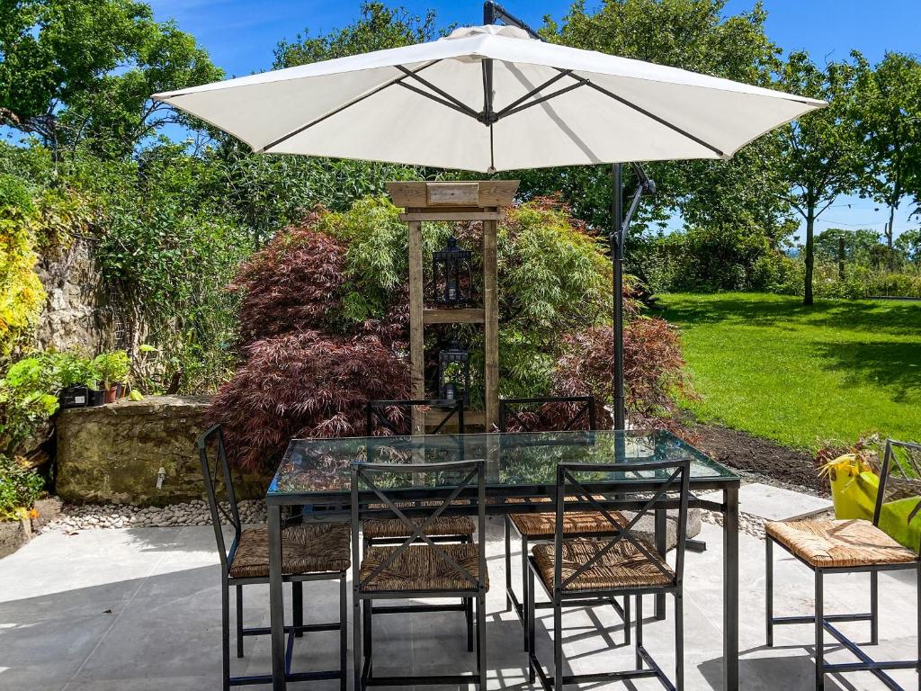 a glass table with an umbrella and chairs at North End Cottage in Longframlington