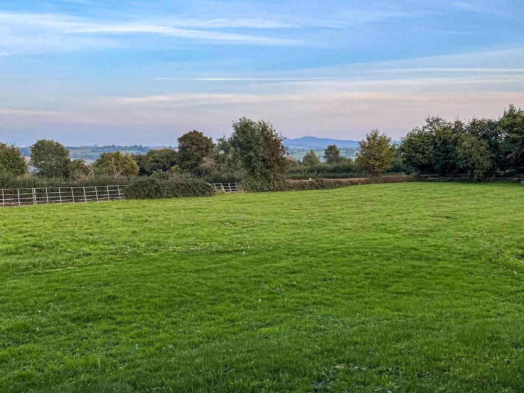 a large green field with trees and a fence at Stable Lodge At Greenacre in Bromyard