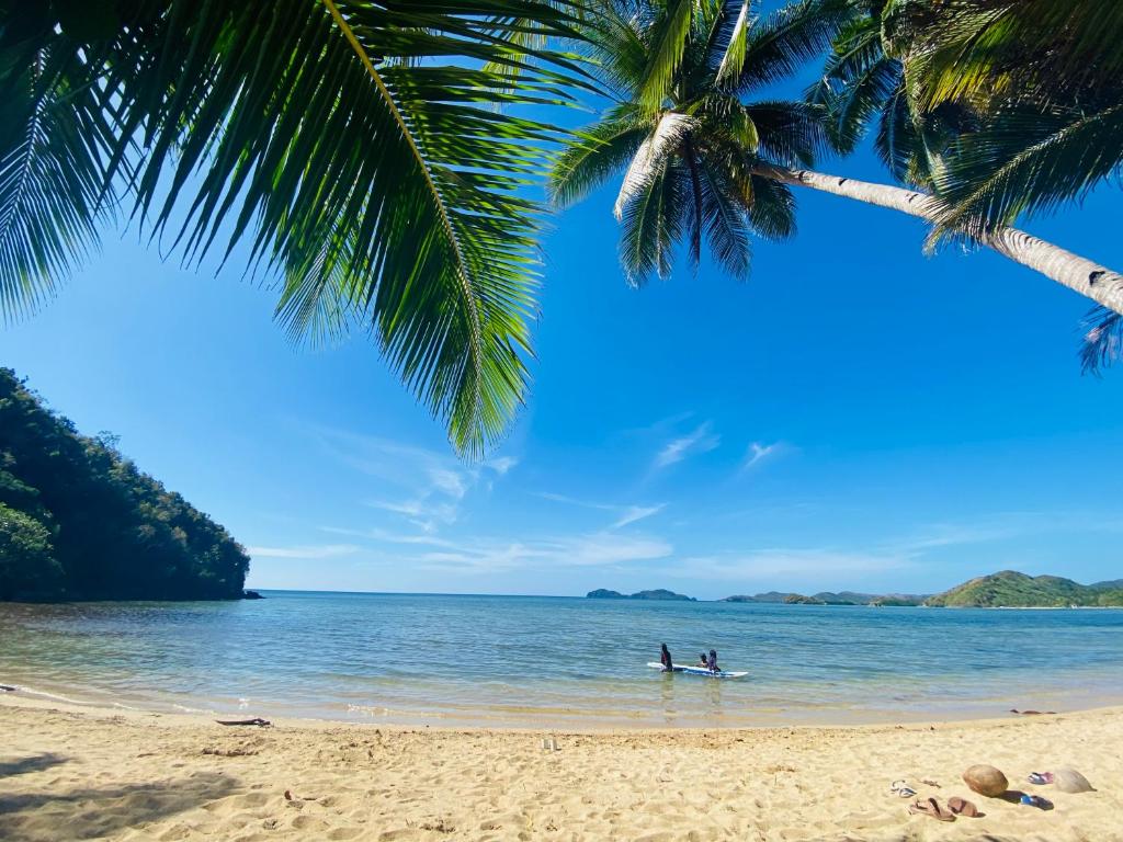 una persona en una tabla de surf en el agua en una playa en Ocamocam Beach Martins en New Busuanga