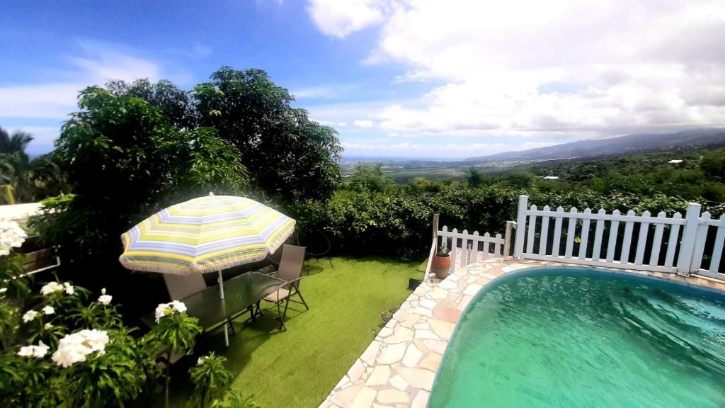 una piscina con sombrilla, mesa y sillas en Le gîte du pavé, en Saint-Paul