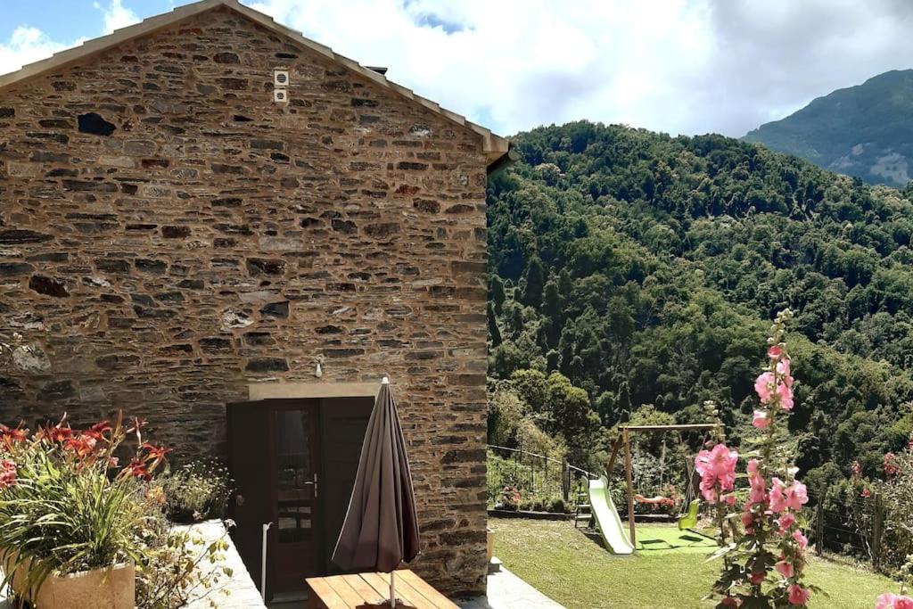 un bâtiment en briques avec un parasol à côté d'une montagne dans l'établissement Maison de charme Orezza Haute-Corse Castagniccia, à Carpineto