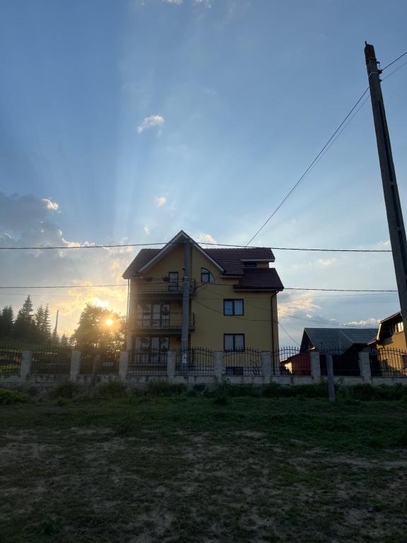 a yellow house with the sun setting behind it at Pensiunea Matis Mărișel in Mărişel