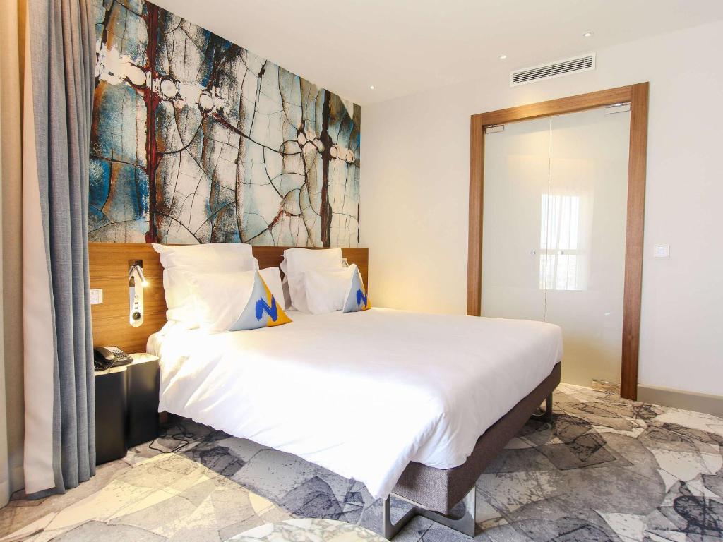 a bedroom with a large white bed with a painting on the wall at Novotel Tunis Lac in Tunis