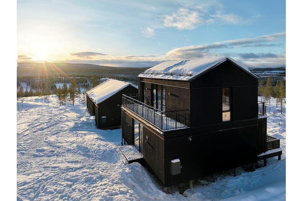 zwei Hütten im Schnee mit der Sonne im Hintergrund in der Unterkunft The Riverside Mountain Lodge - 110sqm of Calm Luxury in Idre