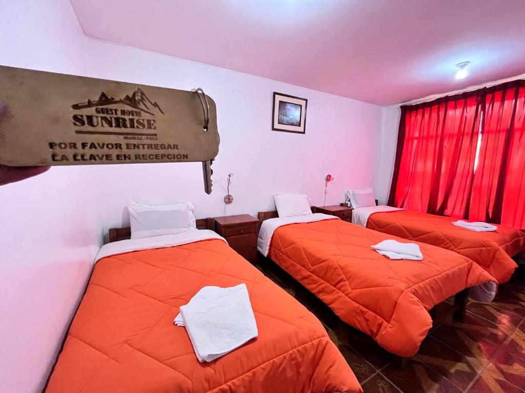three beds in a room with orange sheets at Sunrise Guest House in Huaraz