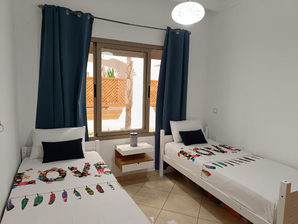 two beds in a room with a window at Appartement de vacances BERALMAR CHEZ HOUDA in Asilah