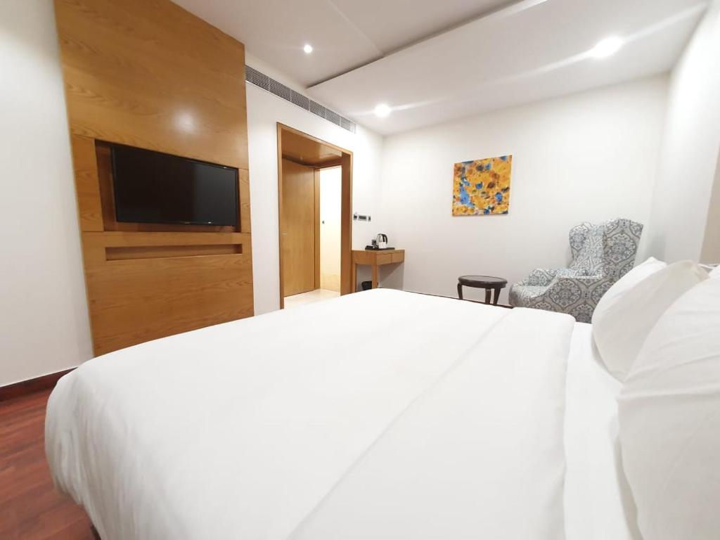 1 dormitorio con 1 cama blanca y TV de pantalla plana en The Moziac Hotel, en Gwalior