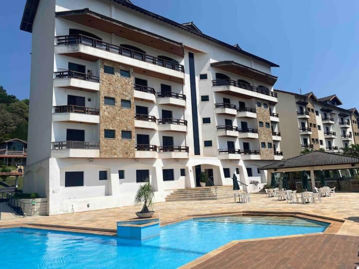 a large building with a swimming pool in front of it at Piemonte Flat Serra Negra in Serra Negra