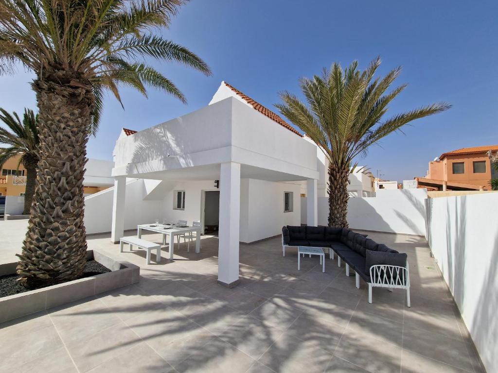 a patio with palm trees and a white house at Hoy Caleta Apartments in Caleta De Fuste