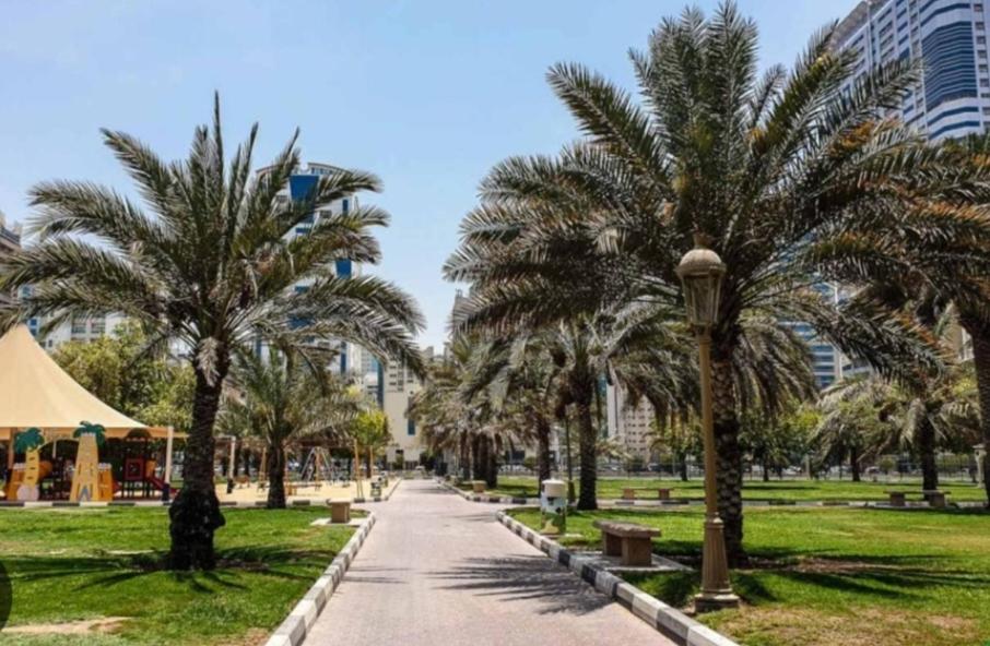 um caminho num parque com palmeiras e edifícios em شقق مفروشة Apartment 2 Bedroom Majaz3 em Sharjah