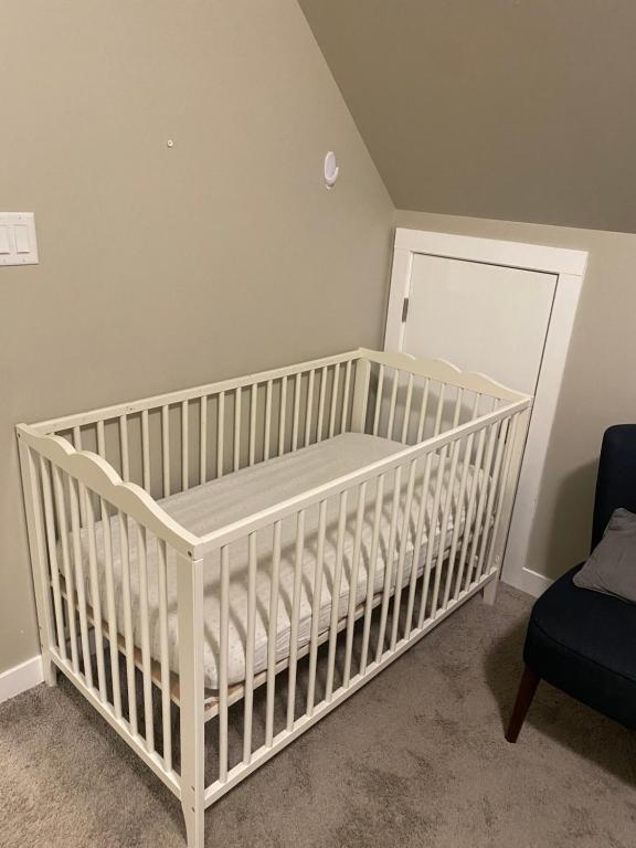 a white crib in a room with a chair at Harbour landing home with 2 living rooms, King bed and 2 car garage in Regina