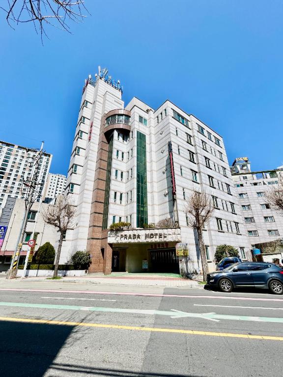巨济Prada motel的一座白色的大建筑,前面有一辆汽车