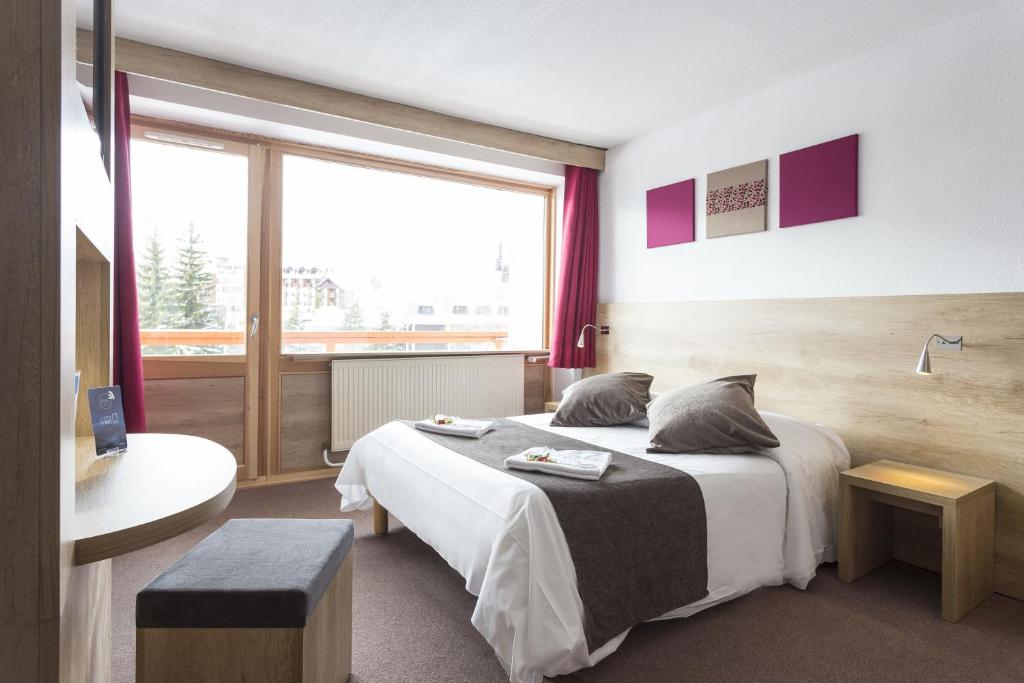 レ・デュー・アルプにあるHôtel Club mmv Le Panorama ***のベッドと大きな窓が備わるホテルルームです。