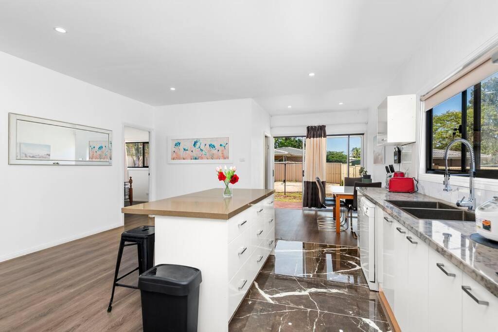 cocina con armarios blancos y encimera en 4Bed Modern Oasis by Train Station, en Wyong