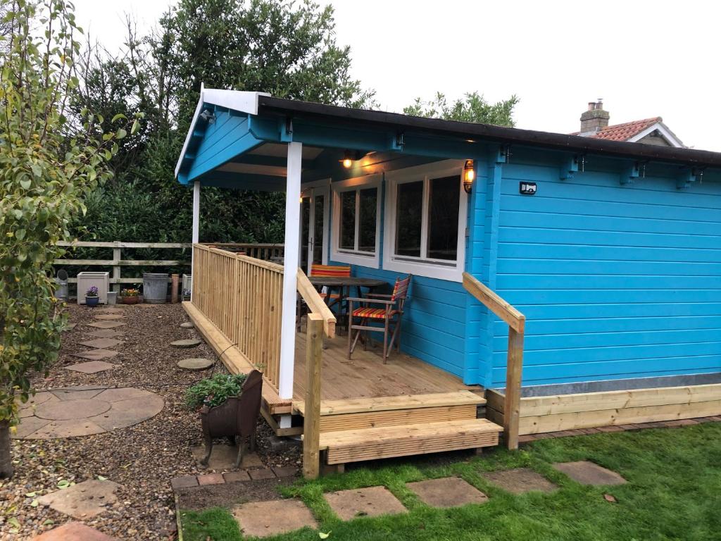 a blue tiny house with a deck with a table at Beckside Lodge in Malton