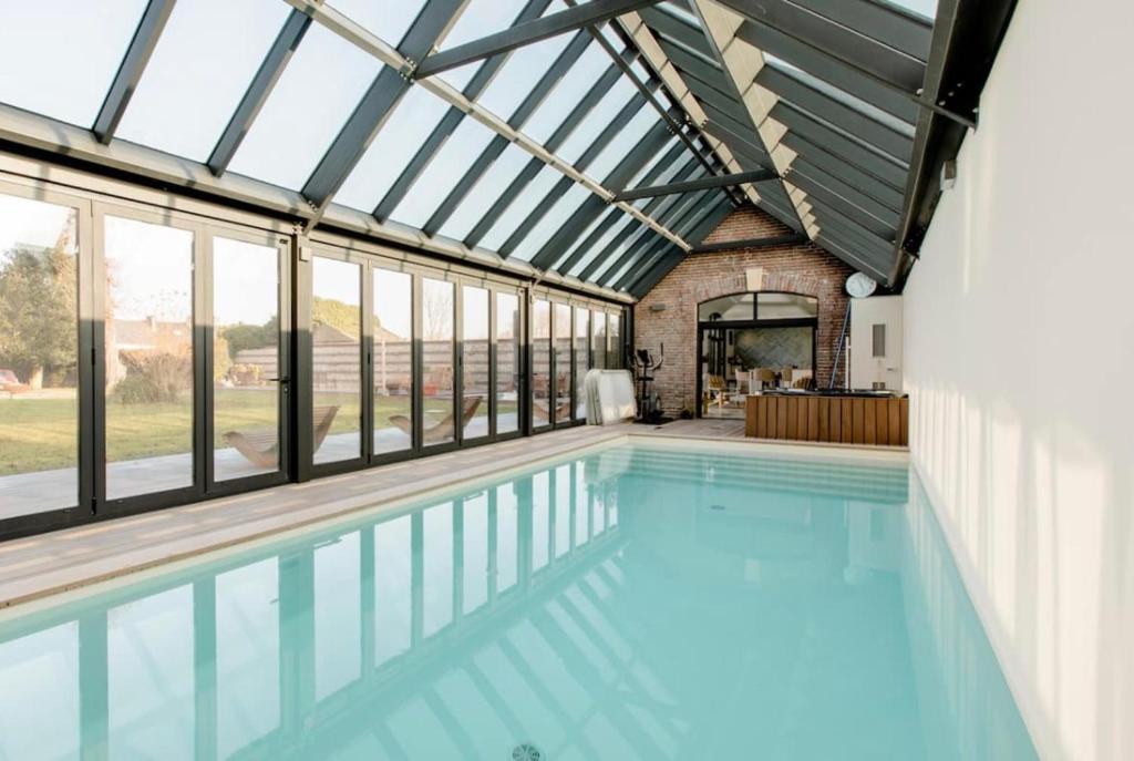une piscine intérieure avec un plafond en verre et des fenêtres dans l'établissement Écurie Les Tourelles Piscine intérieure & spa, à Gainneville